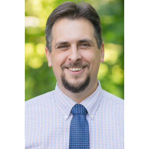 A picture of Jeff Elkins standing in front of green trees.