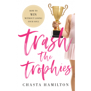 a white background features a dancer in a pink leotard with attached skirt holds a large trophy. a scribbled font says trash the trophies in hot pink. a medallion in the upper lefthand corner holds the tagline: "how to WIN without losing your soul" the bottom of the cover holds the author's name: chasta hamilton. 